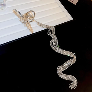 Détail d'une pince à cheveux argentée avec de longs glands en strass sur un plateau rayé