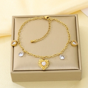 Close-up of golden anklet with heart shell pendant and teardrop zircons on silk