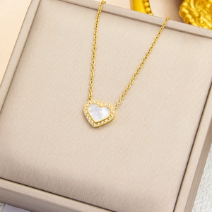 Détail d'un collier cœur doré avec nacre et zircons posé sur un coffret à bijoux chic