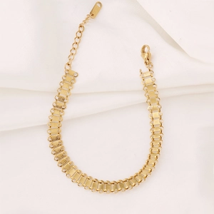 Detailed close-up of a gold ribbed Cuban chain bracelet with lobster clasp on silk fabric