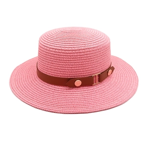Close-up of pink straw hat with brown leather band and gold metal buckle detail