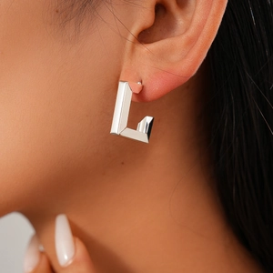 Close-up of minimalist silver geometric C-shaped hoop earrings on a model's ear