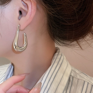 Close-up of a silver polished C-shaped metal earring on a female model’s ear