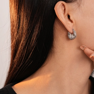 Macro view of silver twisted hoop earring with intricate woven texture on a model