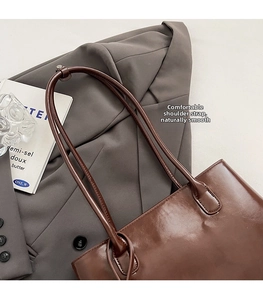 Detail of a brown patent leather shoulder bag styled on a grey suit with accessories