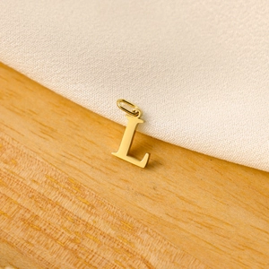 Minimalist gold letter L pendant detail with polished finish and circular bail on wood
