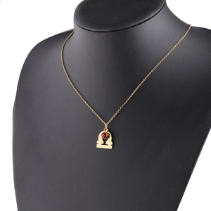 Detailed close-up of gold Libra zodiac necklace with a red gemstone on a black bust model