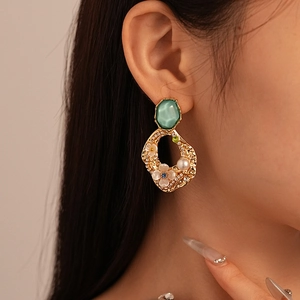 Macro detail of vintage gold flower earrings with green stones and pearls on model