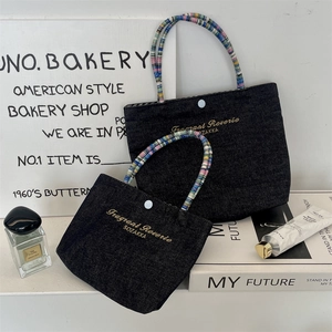 Close-up of denim tote bags with colorful beaded handles and golden embroidered text