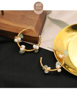 Detail view of handmade gold wire wrapped C-shaped earrings with pearls and green stones