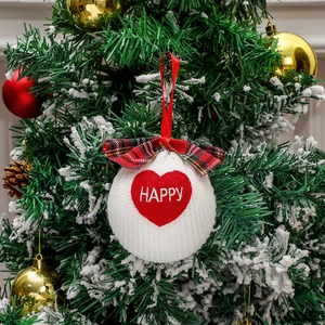 White knitted Christmas ball ornament with red bow and Happy text on a snowy tree