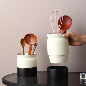 Ceramic kitchen tool holder set with wooden utensils and silicone whisk on a countertop