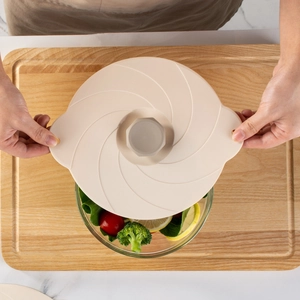 Beige silicone suction lid on a glass salad bowl with fresh vegetables in a kitchen setting