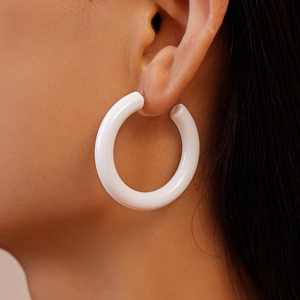 Gros plan de boucles d'oreilles créoles C en acrylique blanc sur modèle, vue de la texture
