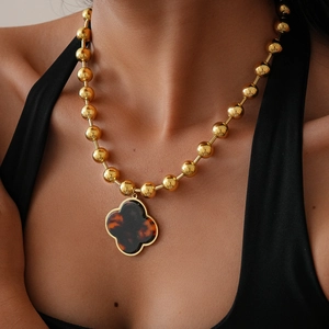 Macro view of gold beaded chain with large amber-textured clover pendant on black top