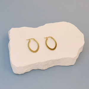 Minimalist gold oval hoop earrings in polished stainless steel on a stone display