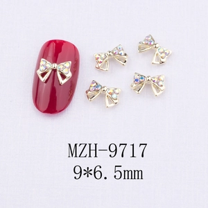 Détail macro du bijou d'ongle nœud doré 9x6,5mm avec strass irisés et cadre ajouré