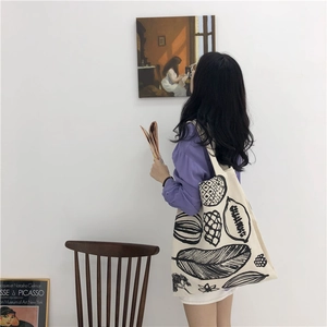 Artistic detail of a cream canvas tote with black botanical prints on a female model