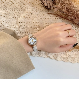 Close-up of elegant women's watch with white shell dial and gold diamond bezel on wrist