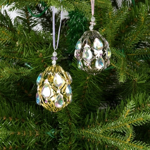 Egg-shaped hollow metal Christmas ornament with iridescent gemstone on tree branch