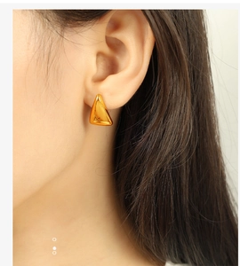 Close-up of a model wearing a geometric gold triangle titanium earring with metallic luster