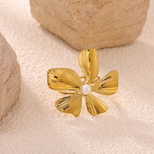 Detailed view of a gold flower ring with white pearl center on a beige textured background