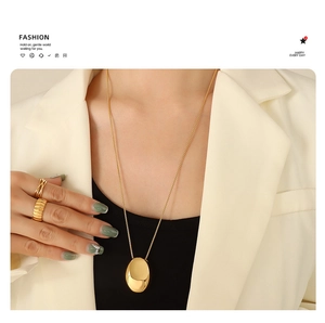 Detail of a minimalist gold-plated oval pendant necklace and matching band ring on a model