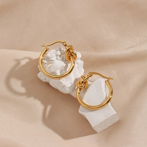 Artistic detail of gold knot earrings on a white plaster bust with beige silk background