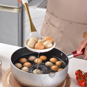 Gold handle white silicone skimmer spoon scooping meatballs in a boiling pot