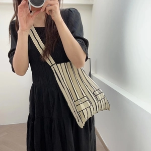 Close-up of beige knitted tote bag featuring black vertical stripes and two pocket details