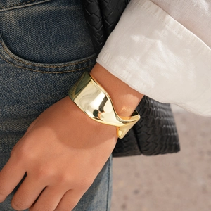 Close-up of a wide twisted gold metal cuff bracelet on wrist with a polished mirror finish