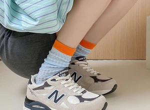 Close-up of blue mesh crew socks with orange cuffs worn with grey sneakers