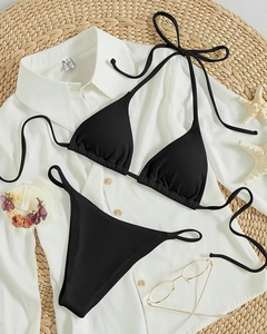 Flat lay of black ribbed halter bikini set on a woven mat with white shirt detail