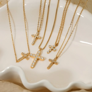 Set of six gold stainless steel cross necklaces with cubic zirconia on a ceramic tray