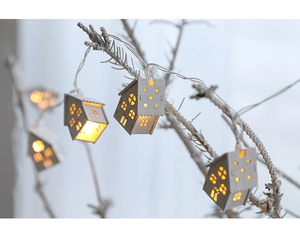 Close-up of wooden house-shaped LED string lights with warm yellow glow on white branches