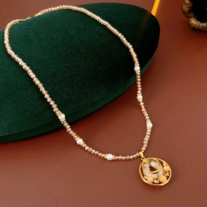 Detail of gold necklace featuring stylized fish pendant with orange beads and pearls