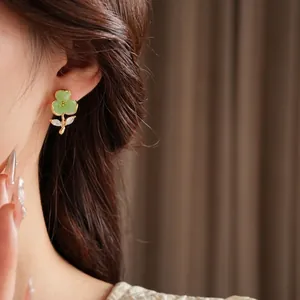 Elegant gold plated flower earrings with green petals and crystals worn by a model
