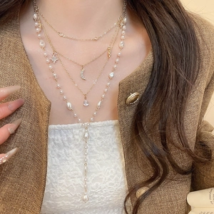 Detail of layered gold necklace with diamond star moon pendants and white pearls