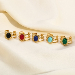 Close-up of five gold open rings with colorful oval natural stones on silk fabric