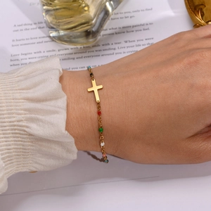 Close-up of golden stainless steel cross bracelet with colorful beads on a model's wrist