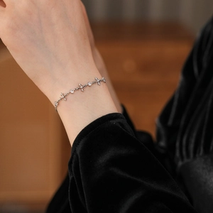 Detail of zircon cross bracelet in silver finish worn on model with black velvet outfit