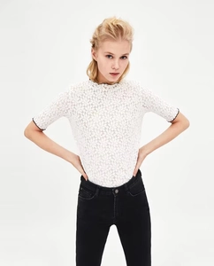 Dettaglio dell'elegante top in pizzo bianco con motivo floreale e bordi neri a contrasto