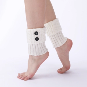 Detail of white cable knit leg warmers with decorative black buttons on ribbed cuffs