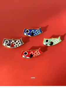 Set of four colorful koi fish enamel pins in red, blue, black, and green on red background