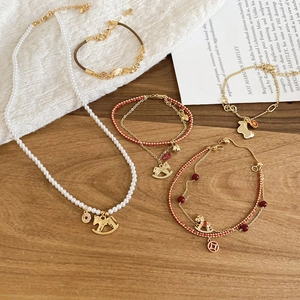 Detailed set of zircon horse pearl necklace and red cord bracelets on wood table