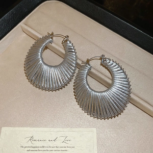 Détail des créoles géométriques tissées en argent dans un écrin à bijoux noir élégant