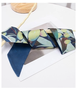 Detail of silk-like neck scarf with yellow olive print wrapped on a wooden branch