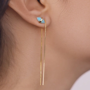 Close-up of a minimalist gold tassel ear thread with light blue geometric charm on model