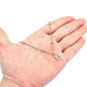 Hand holding silver stainless steel necklace with bead accents and letter M pendant