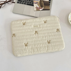 Close-up of cream quilted laptop sleeve with cute rabbit embroidery and brand woven label
